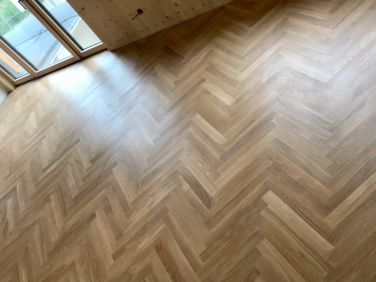 Parkett Heller Parkettboden im Fischgrätmuster in einem Raum mit großen Fenstern.