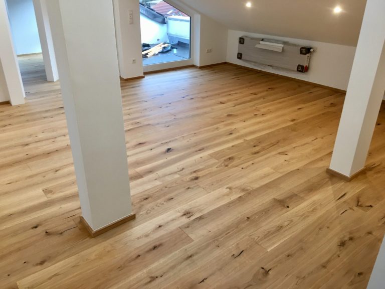 Reinigung, Pflege Holzfußboden in einem hellen Raum mit weißen Wänden und großen Fenstern.